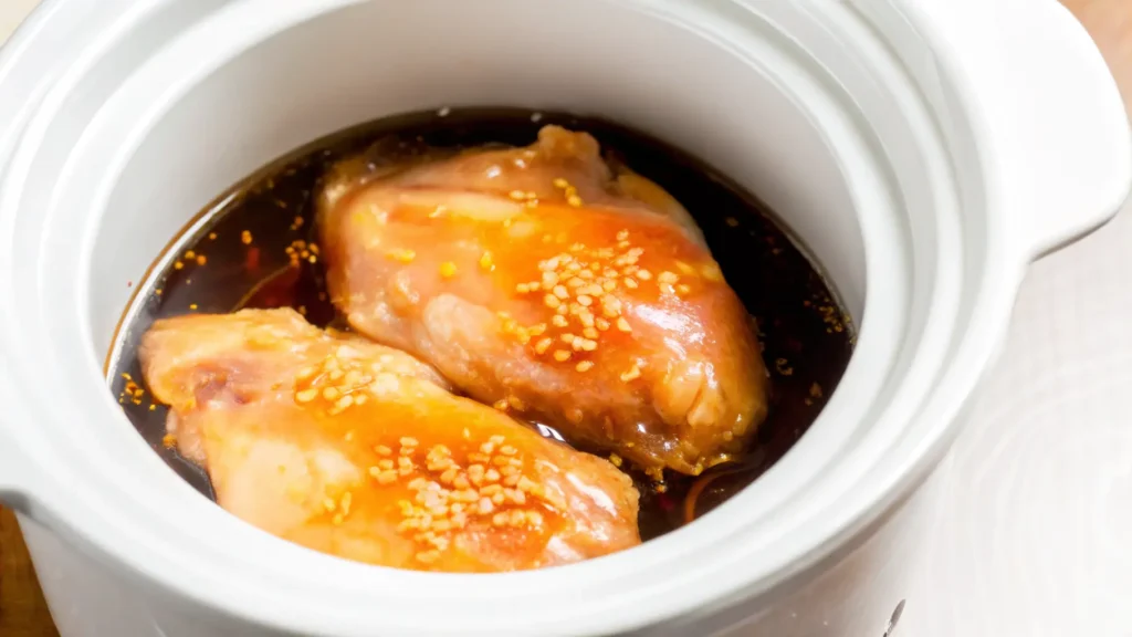 A bowl of slow cooker teriyaki chicken served over steamed rice with sesame seeds and green onions.